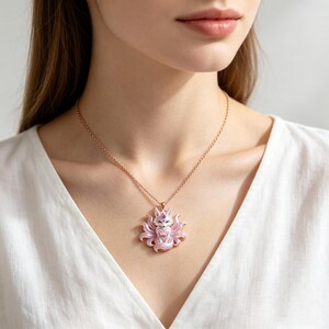 May include: A rose gold chain necklace featuring a pendant shaped like a nine-tailed fox. The fox is finished in iridescent light pink and white enamel with a small purple gemstone set on its forehead and a pink stone held in its paws.