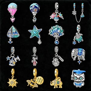 Puede incluir: Colección de abalorios de plata con varios diseños, incluyendo un globo aerostático, un velero, una estrella de mar, helado y un elefante. Los abalorios presentan esmalte de colores y detalles de cristal, algunos con temas de graduación.