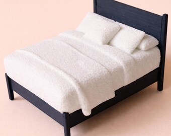 May include: A miniature navy blue bed with white bedding and pillows. The bed frame has a simple design with a headboard and four legs. The bedding includes a fluffy white blanket and two pillows, creating a cozy and inviting look.