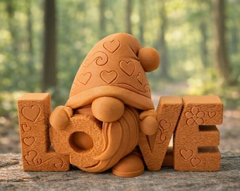 May include: A terracotta-colored gnome figure with a heart-patterned hat and beard, holding the letters "LOVE". The letters and gnome are decorated with hearts and floral designs. The scene is set outdoors with a blurred forest background.