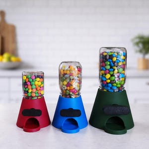 May include: Three candy dispensers with glass jars filled with colorful candies. The dispensers are red, blue, and green, each with a dispensing slot. The jars sit atop cone-shaped bases, offering a fun and functional design.