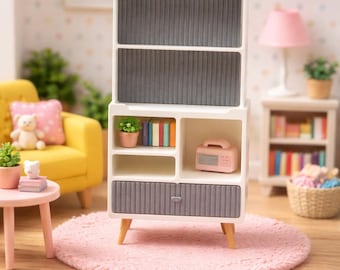 May include: A miniature white and gray cabinet with a mid-century modern design. The cabinet has open shelves, a drawer, and a radio. The cabinet is set on a pink rug, with a yellow chair and a small table in the background.