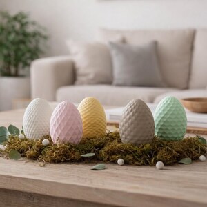 Puede incluir: Cinco huevos de Pascua decorativos en blanco, rosa, amarillo, gris y verde, cada uno con una superficie texturizada. Descansan sobre un lecho de musgo y están dispuestos sobre una mesa de madera, creando un centro de mesa primaveral.