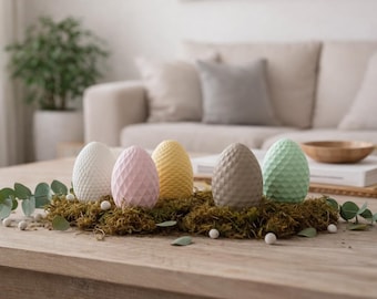 May include: Five decorative Easter eggs in white, pink, yellow, gray, and green, each with a textured surface. They rest on a bed of moss and are arranged on a wooden table, creating a spring-themed centerpiece.