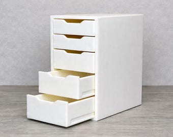 May include: A white, five-drawer storage unit with a rectangular shape. Two drawers are open, revealing a light interior. The unit is made of a solid, opaque material and sits on a gray surface.