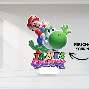 May include: A colorful stand-up decoration featuring Mario riding Yoshi. The design includes the text "JAMES'S GALAXY" in vibrant colors and the option to personalize with a name. The characters are set against a white background.