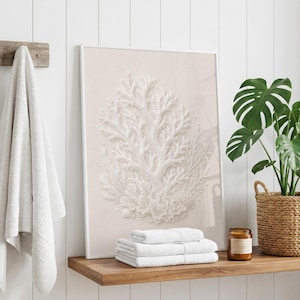 May include: A framed vertical wall art print featuring a white embossed coral reef illustration on a pale beige background, displayed on a wooden shelf with a stack of three folded white towels and a small brown glass candle jar.