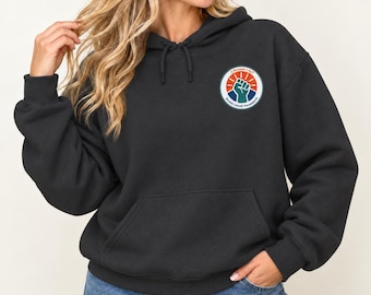 May include: A black hooded sweatshirt featuring a front kangaroo pocket and a circular graphic on the left chest. The graphic displays a raised fist in teal against a blue and orange sunburst background with the text 5 Monate LAUT Biofeedback Therapie.