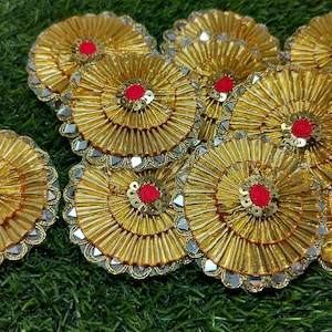 May include: A collection of circular gold fabric patches featuring pleated metallic ribbon, a central red fabric circle, and a border of small reflective mirror-like accents. Each patch has a layered, fan-like texture with gold sequins.