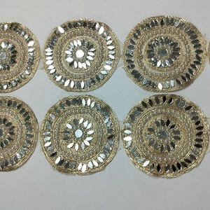 Puede incluir: Un adorno decorativo con un patrón repetido de adornos circulares dorados. Cada círculo está intrincadamente detallado con acentos espejados y un diseño central, creando un efecto brillante. Adecuado para diversos proyectos de manualidades.