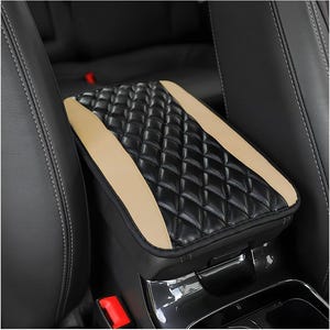 May include: Black and tan quilted car armrest cover. The armrest cover has a diamond pattern and tan side panels. The cover is installed in a car between the front seats.