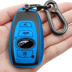 May include: A blue car key fob with black accents and a black carabiner clip. The key fob has several function buttons and a Subaru logo. The carabiner clip is attached to the key fob with a small black ring.