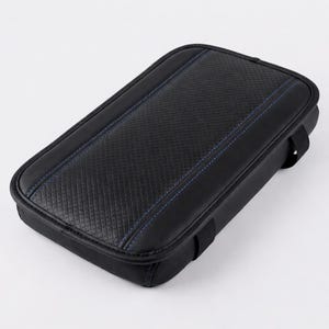 Puede incluir: Apoyabrazos rectangular negro para coche con costuras azules. El apoyabrazos tiene un panel central texturizado con diseño de diamantes y un borde liso y redondeado. Dos correas negras están unidas a los lados.
