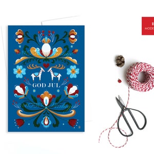 May include: A blue Christmas card with a traditional Scandinavian folk art design featuring reindeer, flowers, and the text "God Jul" which means "Merry Christmas" in Swedish.