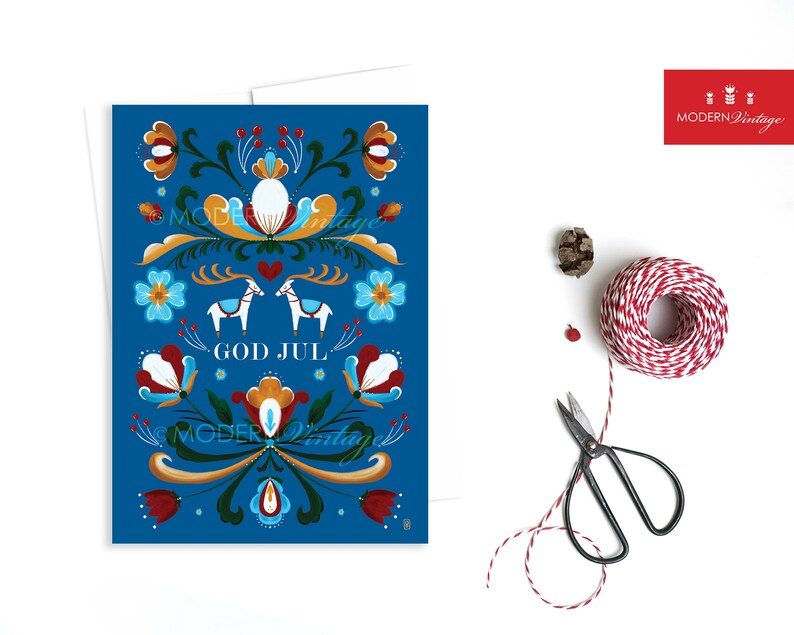 May include: A blue Christmas card with a traditional Scandinavian folk art design featuring reindeer, flowers, and the text "God Jul" which means "Merry Christmas" in Swedish.