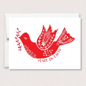 May include: A white greeting card featuring a red linocut-style illustration of a bird holding a leafy branch. The bird has decorative floral patterns on its wing and tail. The text PEACE ON EARTH is printed in red below the bird illustration.
