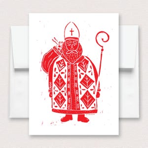 May include: A white greeting card featuring a red linocut illustration of Saint Nicholas. The figure wears a mitre with a cross, a long robe with a diamond leaf pattern, and carries a sack and a staff. The text ST. NICHOLAS is printed at the bottom.