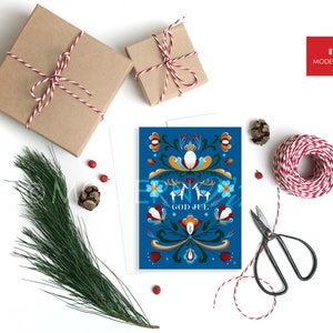 May include: A blue Christmas card with a traditional Scandinavian folk art design featuring a floral pattern, two reindeer, and the text "God Jul".