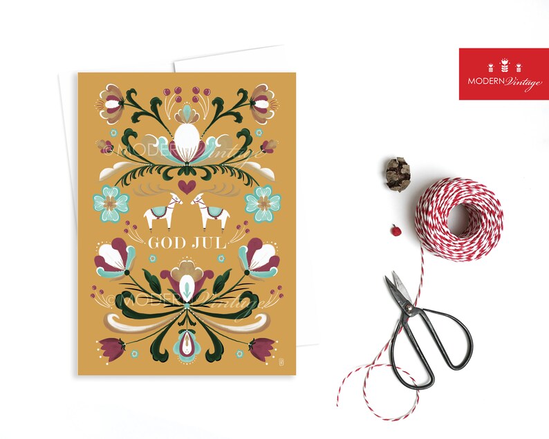 May include: A yellow Christmas card with a Scandinavian folk art design featuring stylized flowers, a heart, and two white horses. The text "God Jul" is written in white.