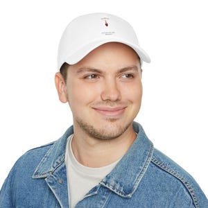 May include: White baseball cap with a curved brim. The cap features a small graphic of a heart and a stylized drawing of a wine glass. The text "TITAN HEART PRINTS" is printed below the graphic. The cap is made of a soft fabric.