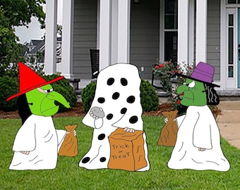 May include: Three Halloween yard decorations featuring two green-skinned figures in white robes and a central ghost figure with black spots. The ghost holds a brown bag labeled Trick or Treat, while the other two figures hold small brown bags.