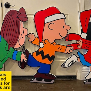 May include: Three Peanuts characters, Charlie Brown, Lucy, and Sally, are depicted as ice skaters. They are wearing winter clothing and hats. The characters are painted on a wooden surface and are ready to be displayed.