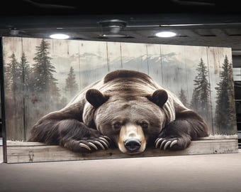 May include: A large canvas print featuring a detailed image of a grizzly bear resting on a wooden ledge. The bear is brown with dark paws and a focused gaze. The background shows a forest scene with mountains and trees.