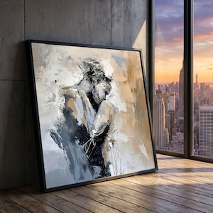 Könnte beinhalten: Abstrakter Kunstdruck in einem schwarzen Rahmen. Das Kunstwerk zeigt zwei sich umarmende Figuren, die in Grau-, Weiß- und Beigetönen dargestellt sind. Das Gemälde lehnt an einer grauen Wand, mit einer Skyline durch ein Fenster.