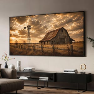 Könnte beinhalten: Ein großes rechteckiges Wandbild mit einer rustikalen Holzscheune und einer Windmühle aus Metall auf einem goldenen Feld unter einem bewölkten Sonnenuntergangshimmel. Das Motiv ist in einem dünnen schwarzen Rahmen eingefasst.