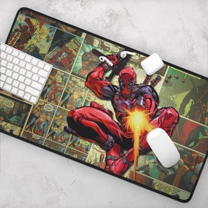 May include: A rectangular mousepad featuring a comic book style design with Deadpool in a dynamic pose, holding a gun and firing a blast. The pad has a black border and a white keyboard and mouse are visible.