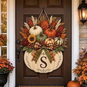 May include: A decorative door wreath featuring a collection of faux pumpkins in white, orange, and green, accented with sunflowers, wheat stalks, and autumn leaves. A large plaid bow sits above a wooden pumpkin cutout displaying the letter S.
