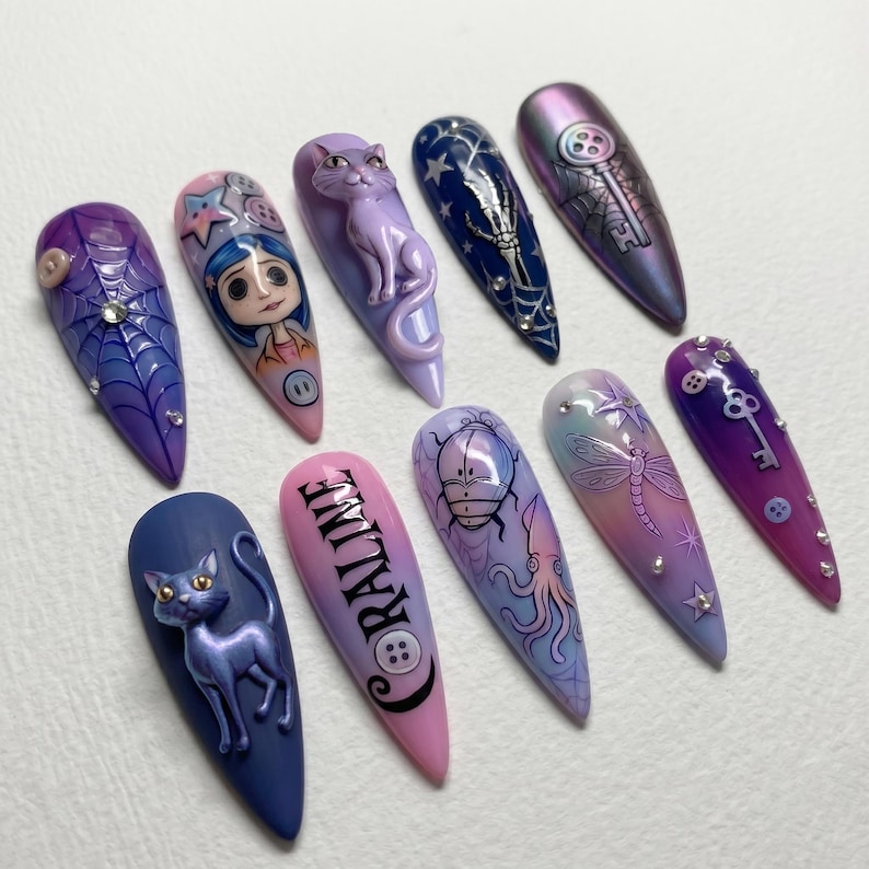May include: A set of ten long, almond-shaped artificial nails with various designs. The designs include a spiderweb, a cartoon character, a cat, a skeleton, a key, and the word "CORALINE". Colors include purple, blue, pink, and iridescent shades.