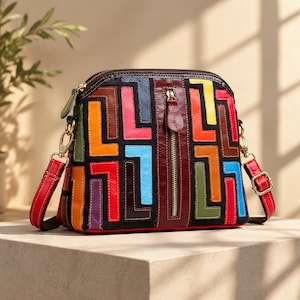 Puede incluir: Un bolso bandolera en forma de cúpula con base negra y un patrón geométrico de parches de cuero multicolor en rojo, naranja, amarillo, azul, verde y marrón. Incluye un bolsillo frontal vertical con cremallera y una correa roja ajustable.