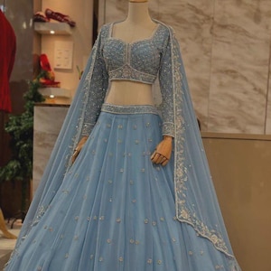 May include: A pale blue formal gown with a matching long-sleeved top and a flowing skirt. The outfit is decorated with silver embroidery and small, sparkling details. The gown is displayed on a mannequin.