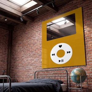May include: A rectangular mustard yellow wall art piece featuring a reflective mirror section at the top and a large white circular control interface below. The interface includes black icons for fast forward, rewind, play, pause, and a heart symbol.