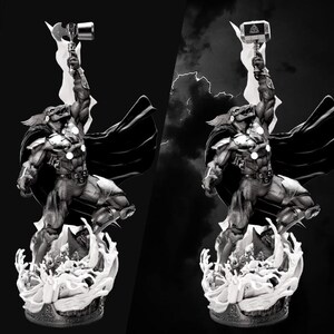 Op de afbeelding: Zwart-wit beeld van een superheld die een hamer omhoog houdt. De figuur staat dynamisch op een gestileerde basis, met een cape die achter hem wappert. Bliksemflitsen op de achtergrond versterken het dramatische effect.