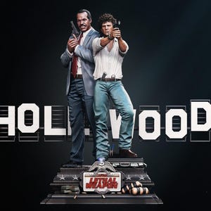 Op de afbeelding: Een gedetailleerd beeld met twee figuren die wapens vasthouden, tegen een donkere achtergrond met het woord "HOLLYWOOD" in witte blokletters. De basis van het beeld toont de tekst "LETHAL WEAPON". De figuren zijn gekleed in pakken en vrijetijdskleding.