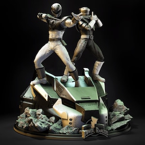 Peut inclure: Une statue détaillée représentant deux figurines de Power Rangers dans des poses dynamiques. L'une est en blanc et noir, l'autre en noir et gris. Elles se tiennent sur une base futuriste avec des détails rocheux, avec le logo Power Rangers.