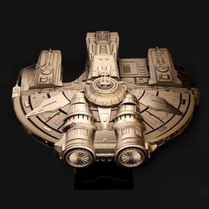 May include: A detailed, metallic model of a spacecraft, featuring intricate paneling and engine details. The model has a circular central section with two prominent cylindrical engines and a rectangular base. The overall color is a muted gold.