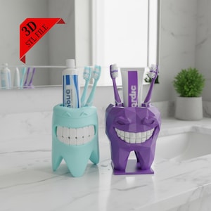 May include: Two novelty toothbrush holders in the shape of teeth, one turquoise and one purple, each with a smiling mouth. The turquoise holder contains a tube of toothpaste and toothbrushes, while the purple holder also holds toothbrushes and toothpaste. A red banner reads "3D STL FILE."