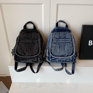 Op de afbeelding: Twee denim rugzakken in verschillende tinten blauw en zwart. Elke rugzak heeft een handvat aan de bovenkant, verstelbare bandjes en een voorvak. De rugzakken zijn gemaakt van stevig denim materiaal en hebben een klassiek ontwerp.