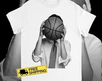 May include: White t-shirt with a black and white graphic of a person holding a basketball in front of their face. The person is wearing a white shirt and a checkered tie. A yellow rectangle with the words "FREE SHIPPING" is at the bottom.
