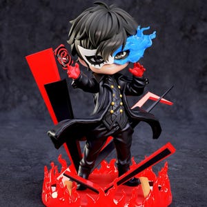 May include: A figurine of a character from the Persona 5 video game. The figure is wearing a black coat, pants, and a mask. The figure is standing on a red base with flames and red and black accents. The figure is holding a card.