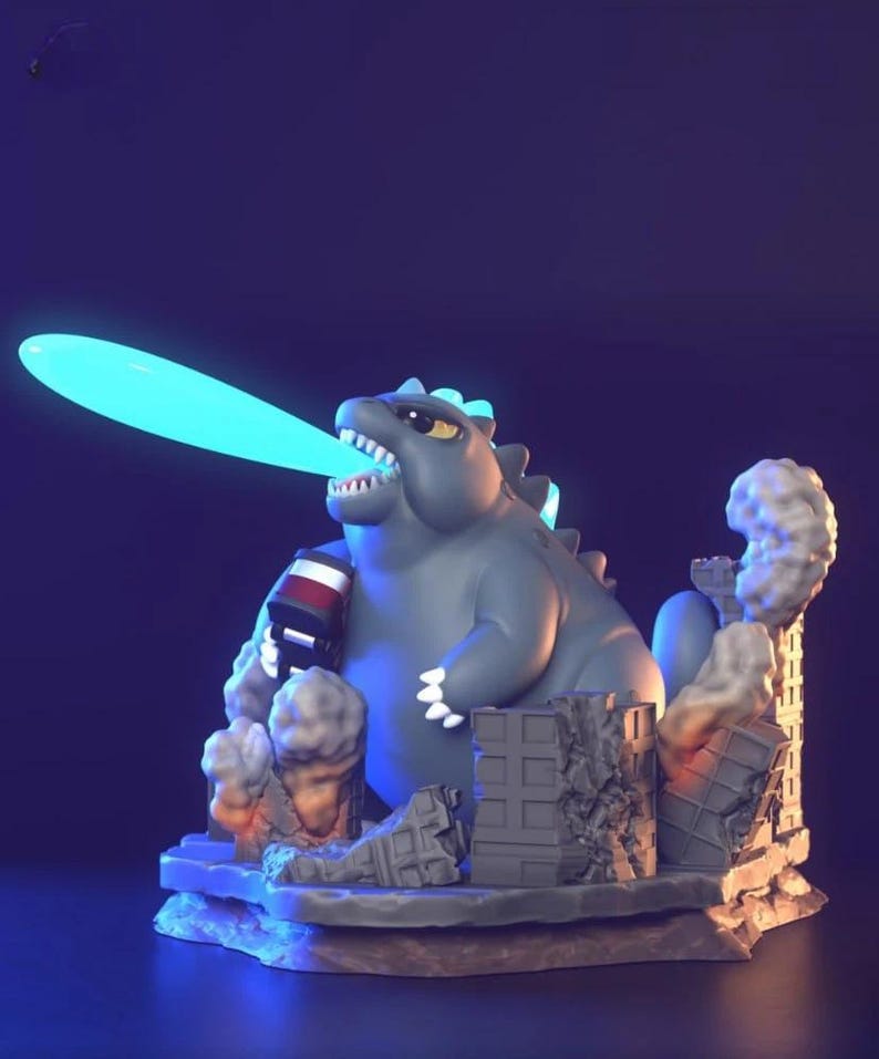 May include: A grey Godzilla figurine with a blue atomic breath effect. The figurine is set on a base with miniature building ruins and smoke effects. The figure is holding a red and white object.