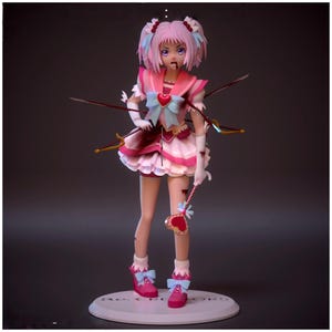 May include: A pink and white anime-style figurine with multiple arrows piercing its body. The figurine has pink hair, a matching outfit with a blue bow, and a heart-shaped accessory. The base reads "RO CRI CORS".