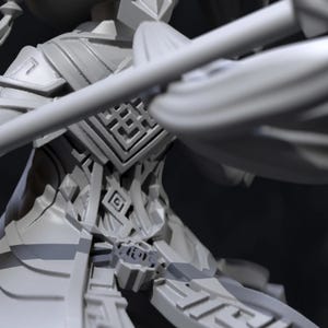 以下が含まれることがあります： 複雑な鎧と幾何学模様を示す、詳細なグレーの3Dプリントフィギュア。デザインは、胸と肩の領域に焦点を当てた、層状の要素を特徴としています。フィギュアは部分的に表示され、背景はぼやけています。