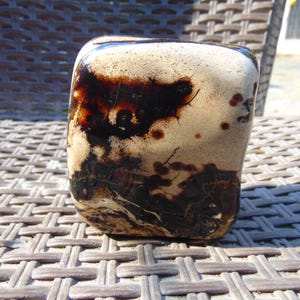 Puede incluir: Una piedra rectangular lisa con bordes redondeados que presenta una base de color crema con manchas de color marrón oscuro, brillantes y de forma orgánica, y patrones intrincados similares a vetas en su superficie pulida y reflectante.