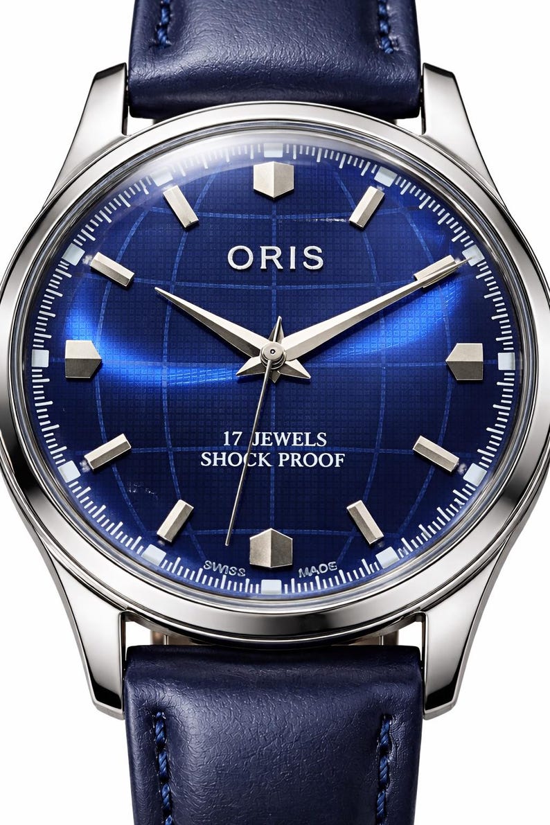 May include: A close-up of a silver-toned wristwatch with a deep blue face. The watch face features the brand name "ORIS", silver hands, and geometric hour markers. The watch has a blue leather band and text that reads "17 JEWELS SHOCK PROOF".