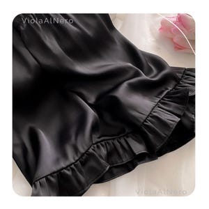 May include: Black satin shorts with a ruffled hem. The shorts have a smooth, shiny texture and are slightly gathered at the waist. The text "ViolaAlNero" is visible in the upper left and lower right corners.