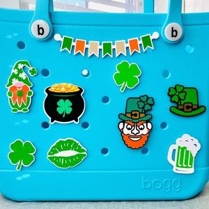 May include: A bright blue tote bag with the word "BOGG" printed on the front. The bag is decorated with various green, orange, and white shamrock and leprechaun themed stickers.